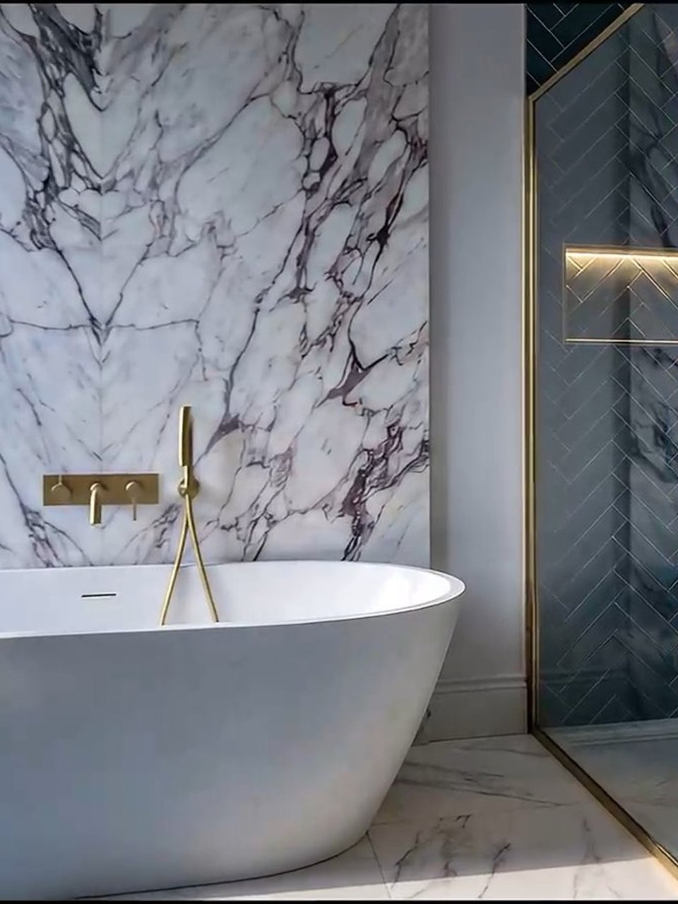 Luxury bathroom in white marble with a freestanding bath, a lit recessed niche and a brushed brass mixer