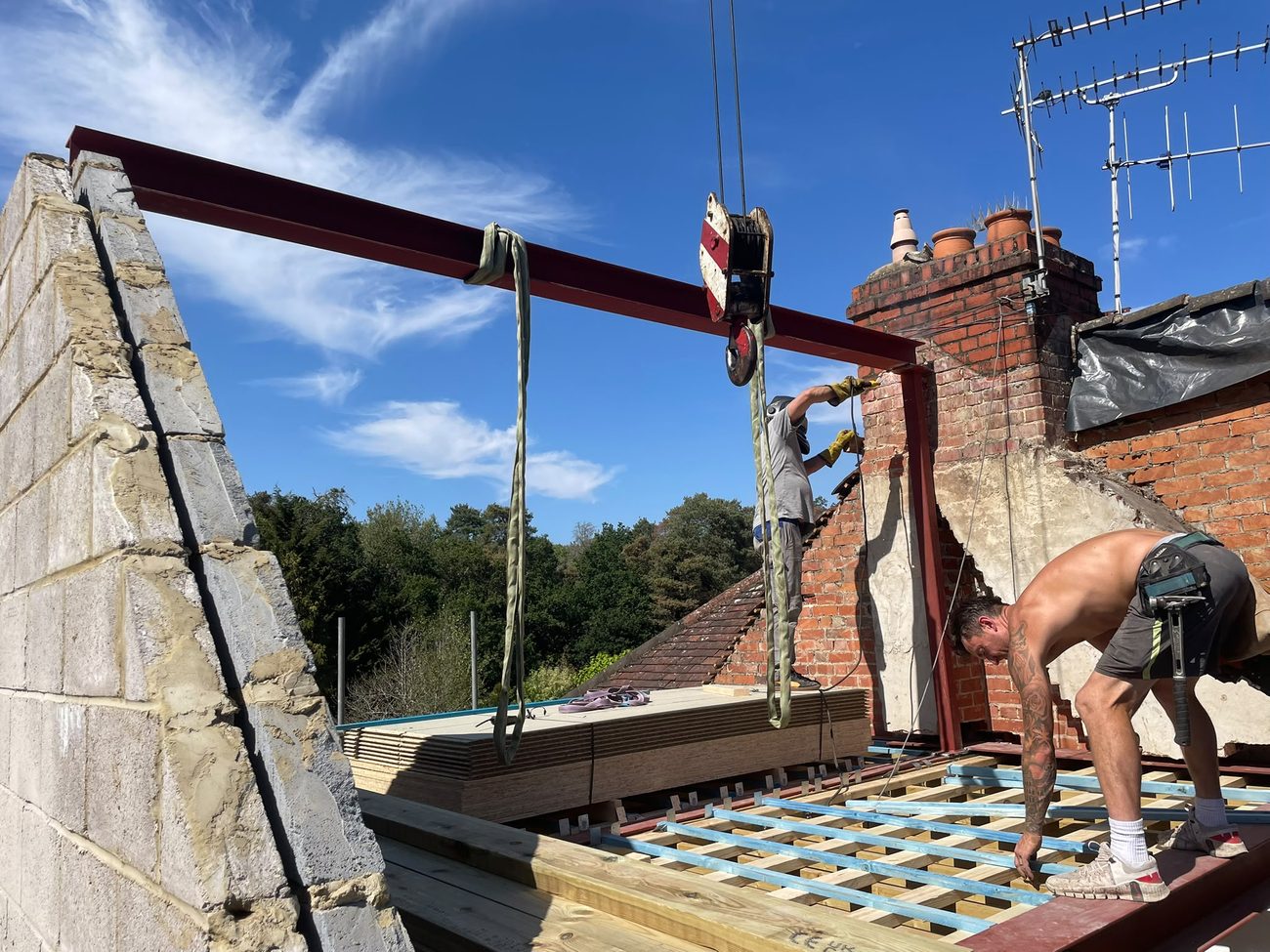 A new structural steel beam craned into place at roof level during a loft conversion, with the RS team fixing it to the chimney breast