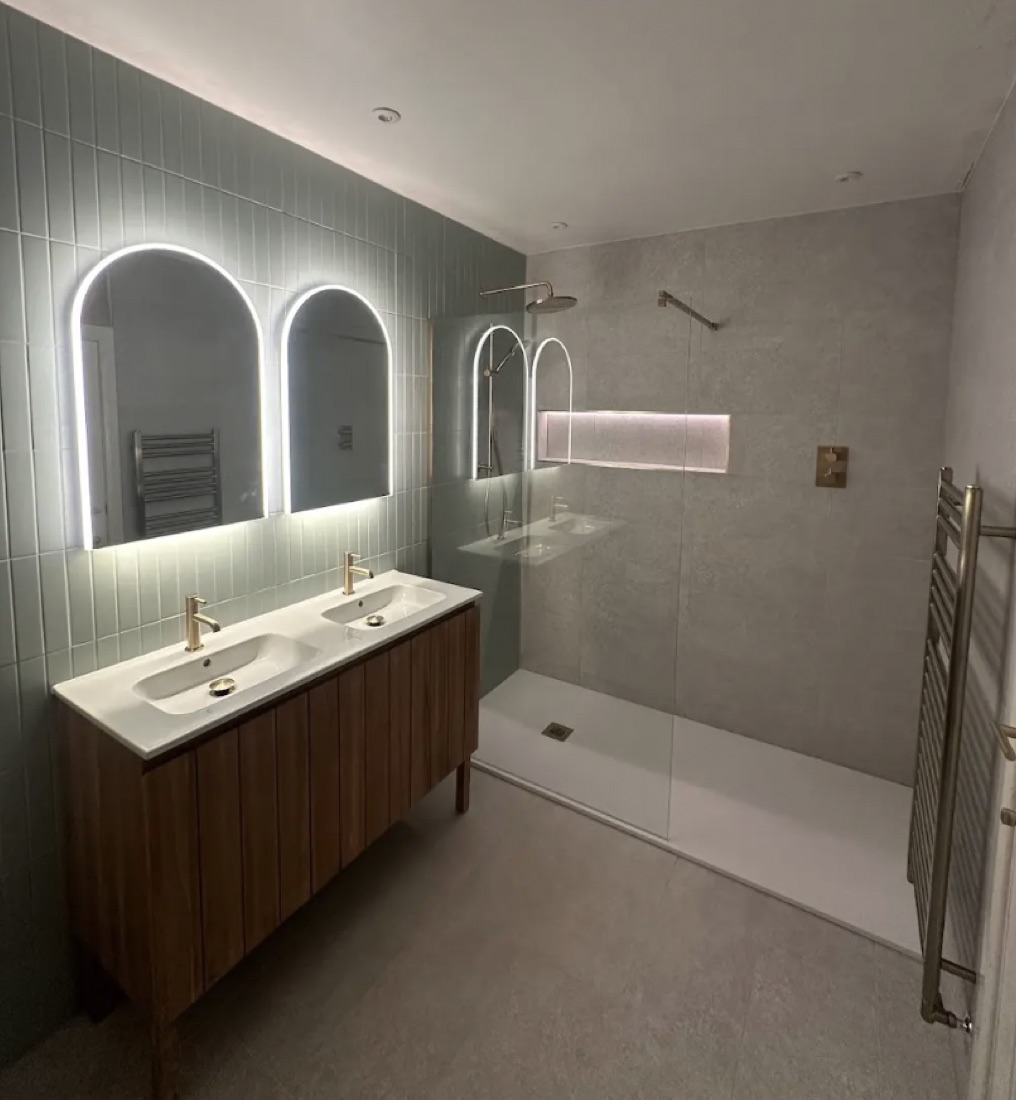 A finished RS ensuite in sage-green tile with twin arched backlit mirrors and a walnut double vanity