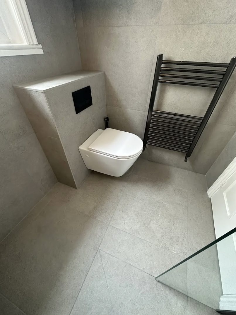 Cloakroom in pale stone tile with a wall-hung WC and a black heated towel rail